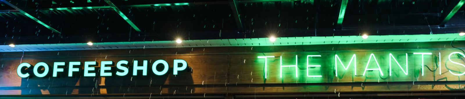 Green neon signs reading 'Coffeeshop' and 'The Mantis' above the shop front